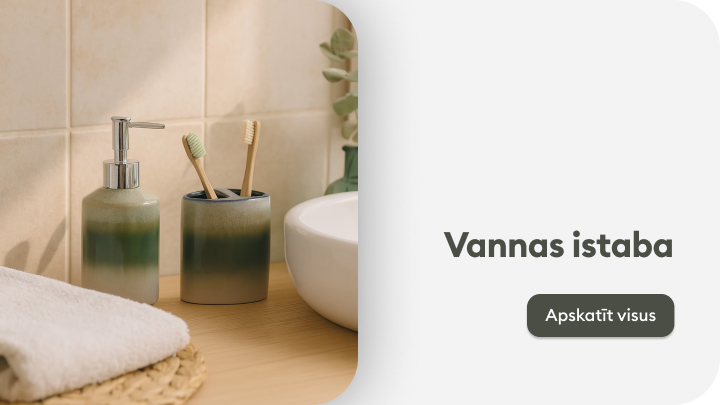 Vannas istaba. Uz koka virsmas novietoti zaļi keramikas trauki – viens ar šķidrā ziepju dozatoru un otrs ar divām zobu sukām. Blakus ir balta keramiskā izlietne un dvielis. Dekoratīvi augi fonā. Tīra un mājīga vannas istabas kompozīcija. banner