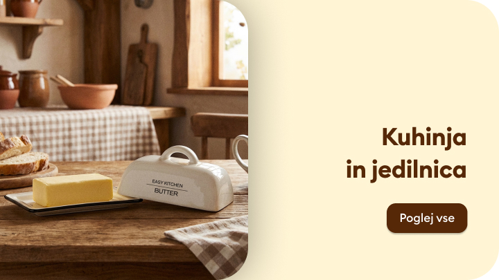 Tradicionalna kuhinja s pogrinjkom na leseni mizi. Na sredini je maslenka s kosom masla in narezan kruh. V ozadju je vidno okno, skozi katerega prihaja naravna svetloba, ter kuhinjski dodatki. Besedilo na desni vabi k ogledu več izdelkov za kuhinjo in jedilnico.