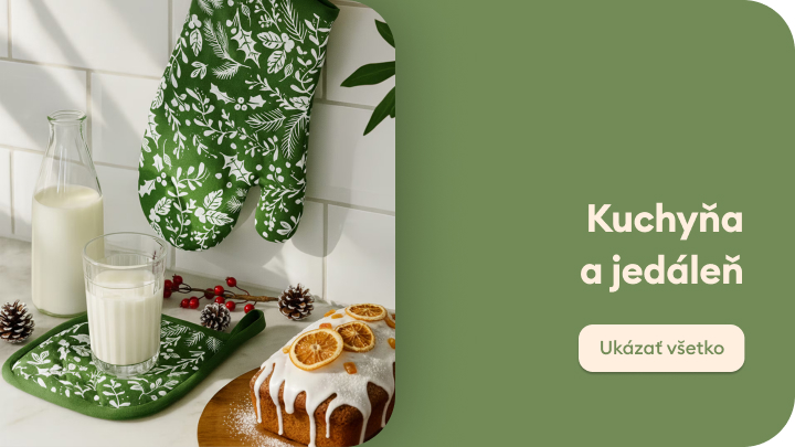 Pečený koláč zdobený polevou a sušenými pomarančmi na kuchynskom stole vedľa pohára mlieka, sklenenej fľaše a kuchynskej rukavice s listovým vzorom. Scéna navodzuje príjemnú atmosféru domáceho pečenia a útulného stolovania. Ukážka kuchynského vybavenia a dekorácií.