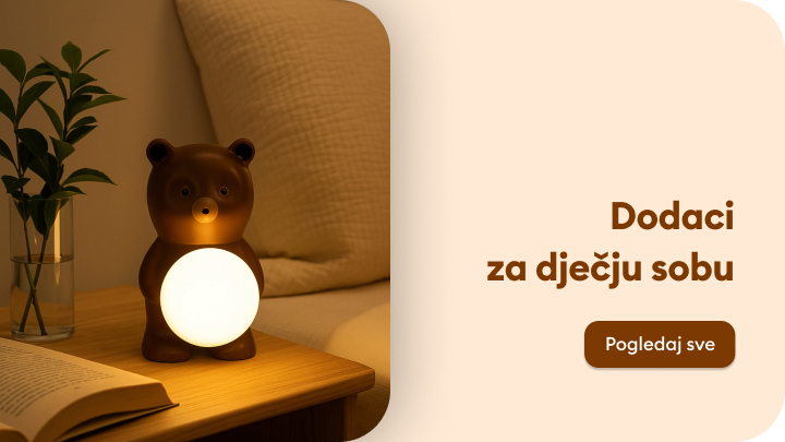 Stolna lampica u obliku medvjeda s mekim svjetlom, idealna za dječju sobu, nalazi se na noćnom ormariću pokraj otvorene knjige i biljke u staklenoj vazi. Tekst na slici poziva na pregled dodataka za dječju sobu, s dugmetom za više informacija. banner