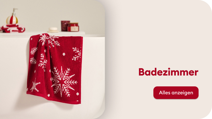 Rotes Handtuch mit Schneeflockenmuster hängt über einer weißen Wanne. Im Hintergrund stehen kleine Badezimmeraccessoires, darunter Seifen und Behälter. Rechts daneben steht der Text „Badezimmer“ mit einem Button „Alles anzeigen“ zum weiteren Erkunden der Kategorie.