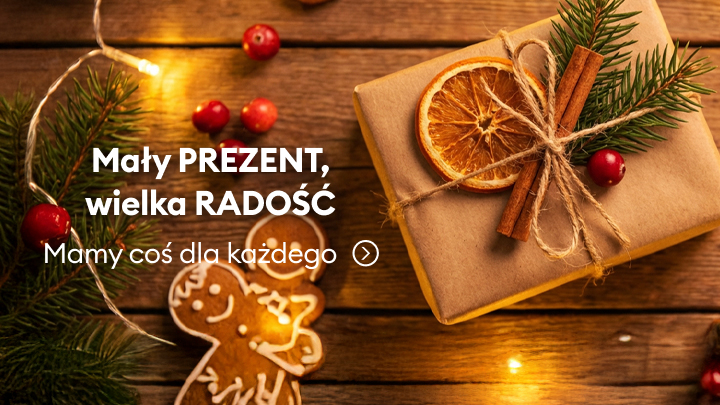 Mały, świątecznie zapakowany prezent ozdobiony suszoną pomarańczą, laskami cynamonu i gałązką iglaka. Obok piernikowy ludzik, gałązki choinki i światełka tworzące przytulną atmosferę. Zachęta: Mały prezent, wielka radość. Mamy coś dla każdego!