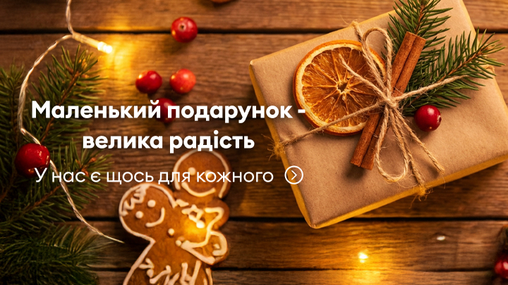 Подарунок, оформлений у святковому стилі: коробка, прикрашена сушеним апельсином, корицею та ялиновими гілками. Поруч новорічне печиво у вигляді пряникової людини та святкові гірлянди. Надпис: «Маленький подарунок – велика радість. У нас є щось для кожного».